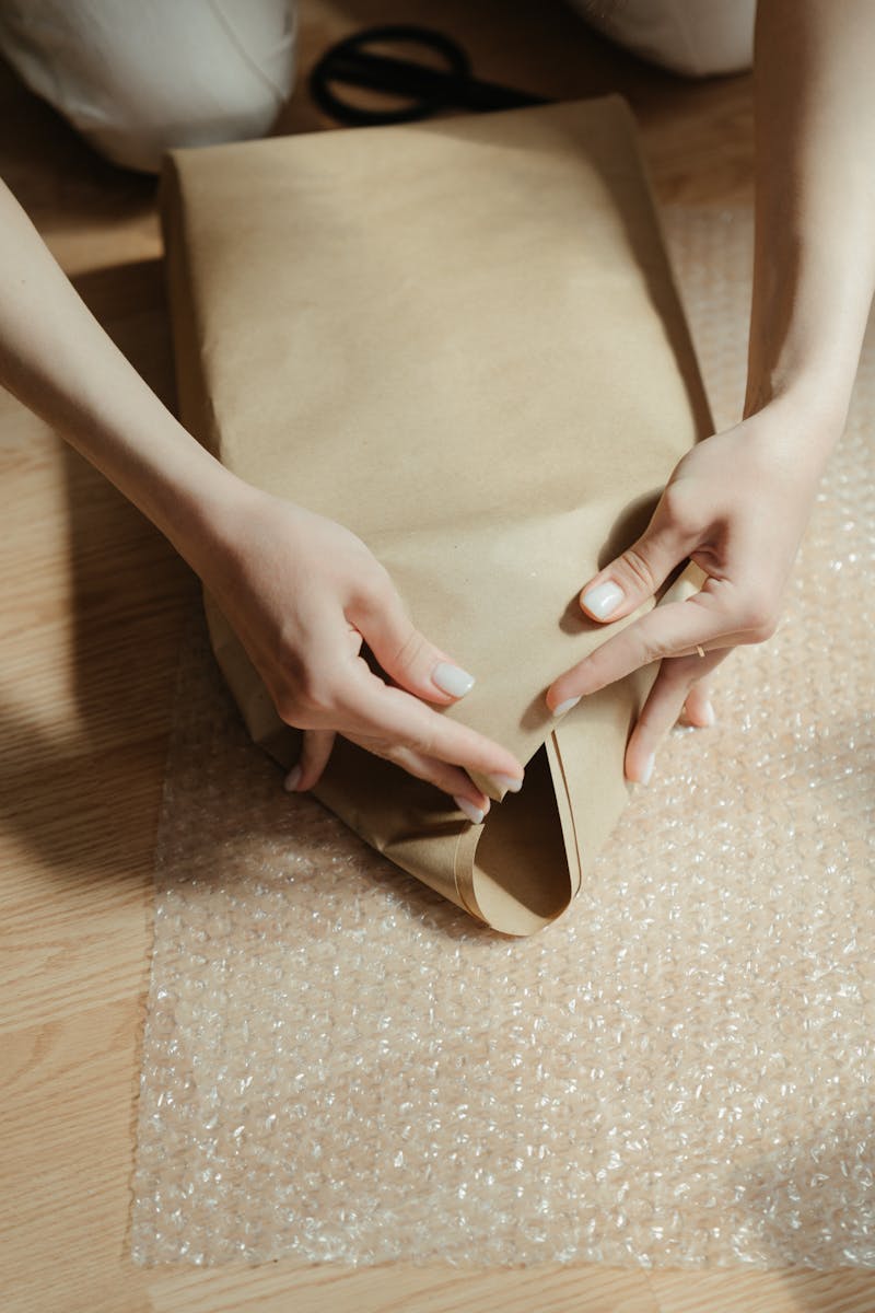 Close-up of hands wrapping a package with protective bubble and kraft paper.